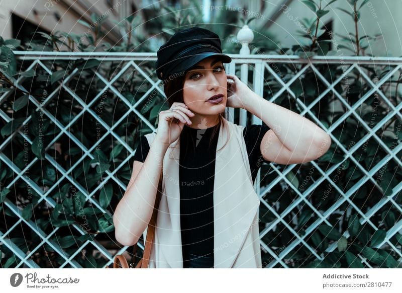 Ziemlich stylische Frau, die eine Kappe aufsetzt. Stil Jugendliche Straße schön Mütze anmachend Zaun Großstadt Mode hübsch attraktiv Model Mensch
