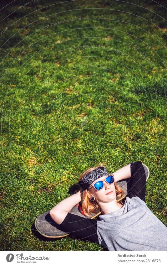 Junge Frau ruht sich im Gras aus, nachdem sie Skateboard geübt hat. Kälte Mädchen Schickimicki Jugendliche Park Licht ruhen lügen Erholung Außenaufnahme Stil