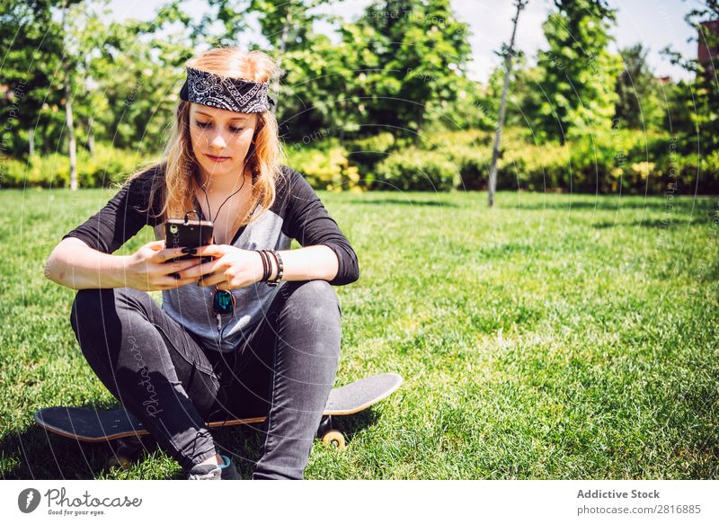 Skateboardfrau beim Musikhören vom Smartphone im Park Kopfhörer Freude PDA Chinese Kultur Handy Außenaufnahme Junge Frau sitzen schwarz Halt Sportbekleidung