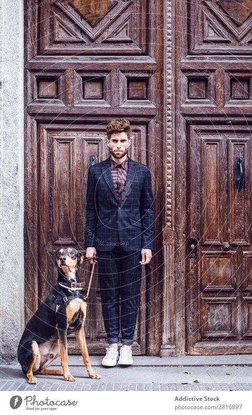 Schöner eleganter junger Modemann im trendigen Kostümanzug mit Hund, alter Holztürhintergrund Anzug Mann Herr modisch Bekleidung Stil Model Hemd Hand lässig