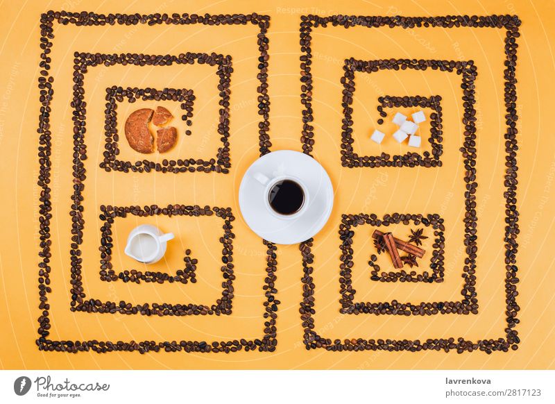 Flachlegung einer Kaffeetasse in der Mitte eines Musters oder Labyrinths aus Kaffeebohnen mit Keksen, Melker, Gewürzen und Zucker Zimt Anissterne