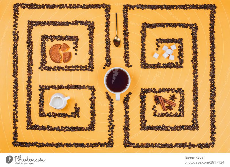 Tasse in der Mitte eines Musters oder Labyrinths aus Kaffeebohnen Zimt Anissterne Kräuter & Gewürze Würfelzucker Plätzchen Keks legen flach gelb Espresso Becher