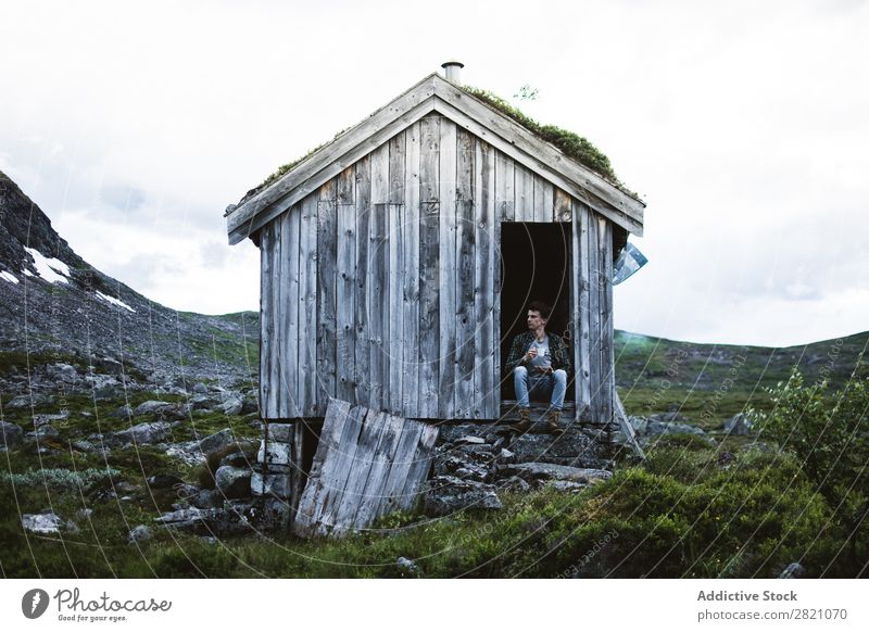 Ein Mann sitzt in einem alten Haus in der Natur. Hütte Berge u. Gebirge abgelegen ruhig Gelände Biegen aber Landschaft friedlich Gebäude Außenseite Idylle