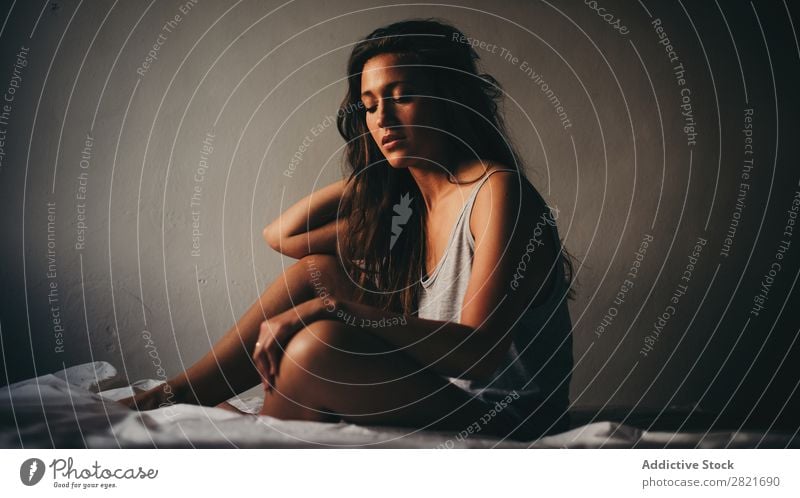 Schöne junge Frau in grau sitzend auf dem Bett schön herabsehend Wand Hintergrundbild itim Intimität Traurigkeit Einsamkeit Körperhaltung Top brünett dünn