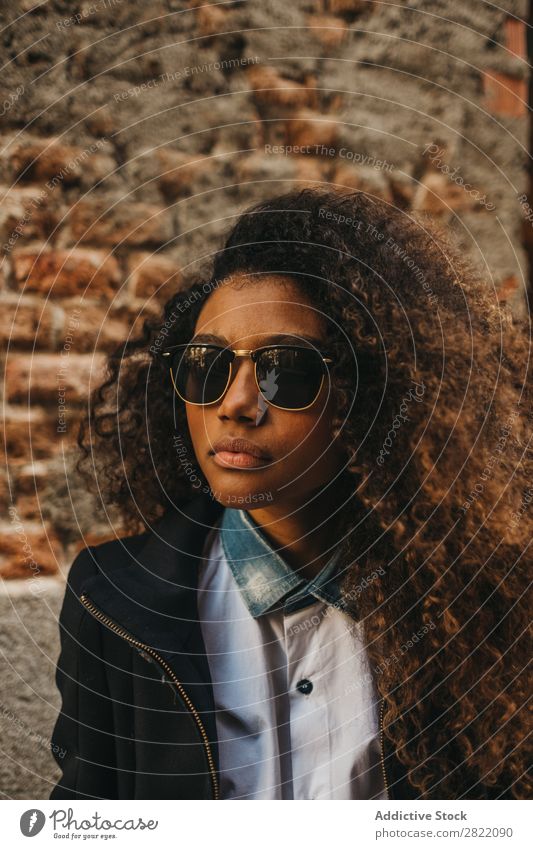 Stilvolle Frau an der Ziegelwand hübsch schön urwüchsig schwarz lockig Afrikanisch Jugendliche stehen Wand Backstein Straße Sonnenbrille brünett attraktiv