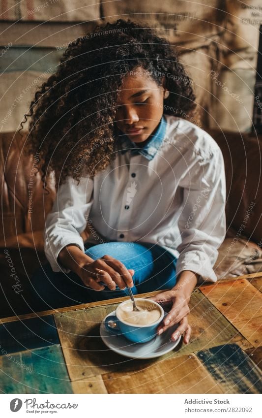 Ethnische Frau, die eine Tasse Kaffee rührt. hübsch schön urwüchsig schwarz lockig Jugendliche rühren Latte brünett attraktiv Mensch Beautyfotografie Erwachsene