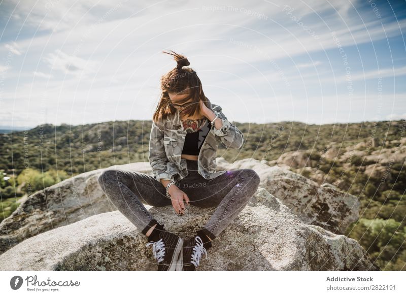 Hübsche junge Frau, die auf einer Klippe sitzt. Stil Natur Felsen Stein Sonnenstrahlen Tag attraktiv schön Jugendliche Mode Schickimicki hübsch Coolness