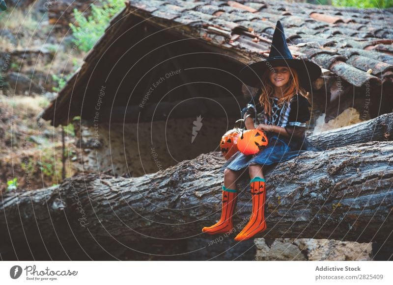 Fröhliches Kind in Kostüm, das auf dem Kofferraum posiert. Mädchen Halloween Körperhaltung Feste & Feiern Tradition Zauberei u. Magie Ausdruck Süßwaren