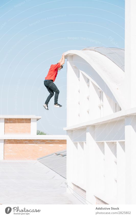 Sportlicher Mann hängend auf dem Dach Sportler Le Parkour Tracer erhängen Klettern Erholung physisch Risiko Dachterrasse Motivation Aktion Läufer Stadt Stunt