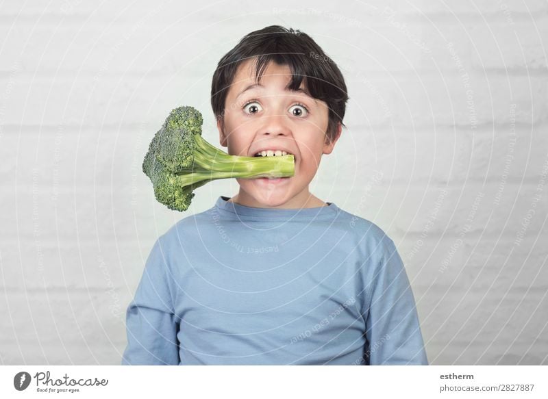 Glückliches Kind mit Brokkoli im Mund gegen Backstein Hintergrund Gemüse Ernährung Essen Mittagessen Vegetarische Ernährung Diät Lifestyle Gesunde Ernährung