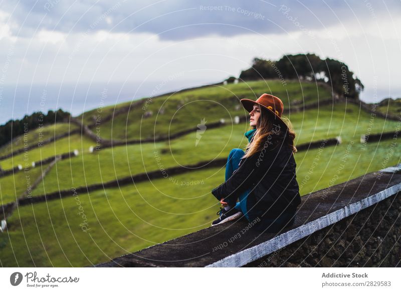 Frau sitzt auf einem Zaun auf dem Feld. sitzen grün Natur Wiese Erholung ruhen Wegsehen Hut Frühling Sommer Gras Landschaft Landwirtschaft ländlich Sonnenlicht