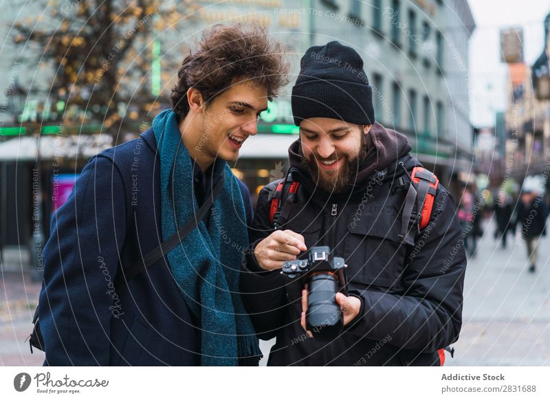 Fröhliche Männer beim Beobachten der Kamera Mann Zusammensein Fotokamera beobachten Ferien & Urlaub & Reisen Tourismus Lächeln heiter gutaussehend Großstadt