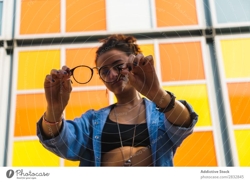 Lächelndes Modell beim Spielen mit einer Brille Frau Körperhaltung spielerisch trendy Straße feminin Ausdruck Accessoire Großstadt Stil Jugendliche Lifestyle