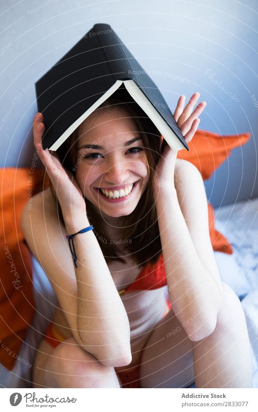Fröhliches Mädchen posiert mit Buch Körperhaltung Bett Kreativität auf dem Kopf Freude Unterwäsche heiter Morgen Schlafzimmer lachen lustig sitzen Geborgenheit