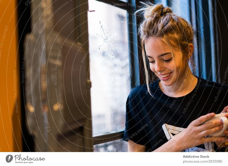 Lächelnde Frau hält einen Becher am Fenster. Tasse Jugendliche schön Beautyfotografie Porträt Mensch Textfreiraum Kaukasier attraktiv hübsch Gesundheit Glück