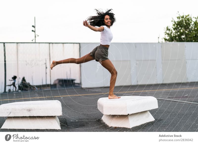 Fröhliche Frau beim Springen hübsch Jugendliche springen sportlich Blöcke Beton gymnastisch Glück heiter Porträt Blick in die Kamera schwarz Afrikanisch Kopf