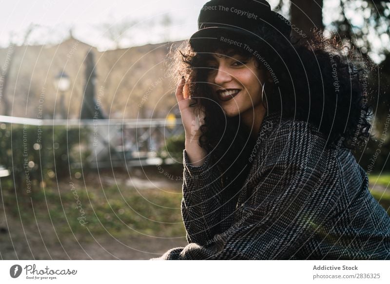 Junge stilvolle Frau, die in der Stadt sitzt. attraktiv Großstadt modisch lockig brünett Mantel Hut sitzen Zaun Aussicht Mode Jugendliche schön hübsch Straße