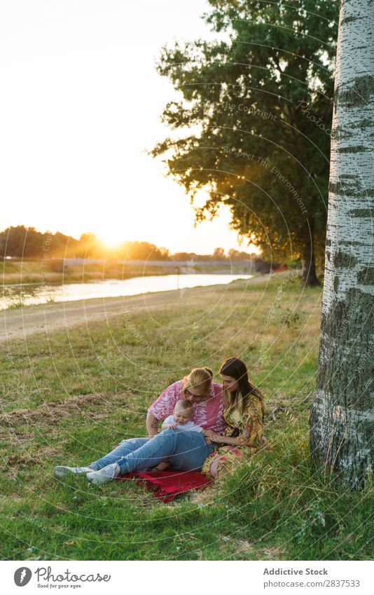 Lesbische Familie mit Kind auf dem Rasen Mutter Park grün Sonnenstrahlen Glück Mensch Frau Fröhlichkeit Sommer Lifestyle Liebe gleichgeschlechtliche Eltern