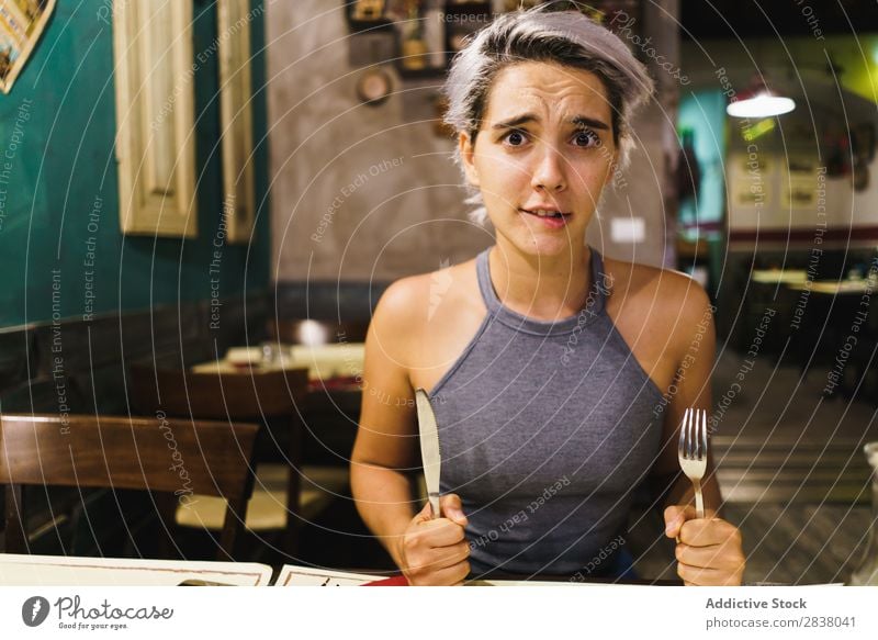 Wütendes Mädchen, das mit Silberwaren posiert. Frau Restaurant Appetit & Hunger Spaß haben Wut Ausdruck Gesichtsbehandlung Gefühle humorvoll hysterisch Café