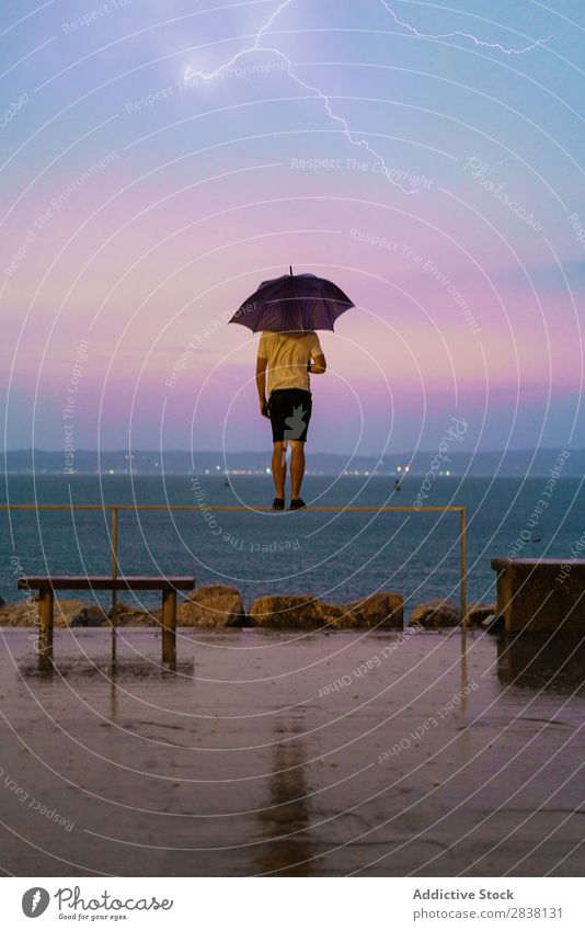 Springender Mann mit Regenschirm in der Natur Körperhaltung Artist Ausdruck Stauanlage Bewegung gymnastisch über der Erde Meer Leistung sportlich