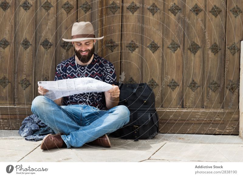 Ein Tourist, der beim Musikhören eine Karte liest und sitzt. Mann Kopfhörer Landkarte Rucksack lesen Wege & Pfade durchsuchend sitzen Ferien & Urlaub & Reisen