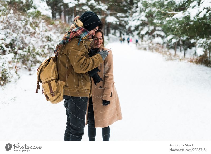 Lachendes Paar mit Telefon im Wald umarmend Winter PDA Zusammensein schön Technik & Technologie romantisch benutzend Internet Schnee weiß Mitbenutzung