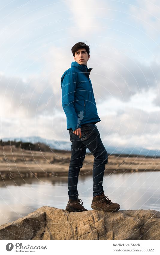 Junger Mann, der gegen den See posiert. Körperhaltung Porträt kalt Stil Erwachsene Landschaft Blick Inspiration ernst stehen modisch Model Außenaufnahme Natur