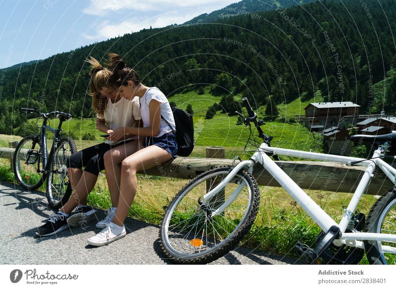 Frauen mit Fahrrädern beim Surfen im Smartphone sitzen Zaun PDA Browsen sportlich Fahrrad Freundschaft Sport Zyklus Mädchen Aktion Lifestyle Fahrradfahren
