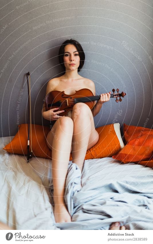 Nackte Frau, die mit Geige posiert. nackt Erotik genießen Musiker deckend sexuell Bett Frauenbrust heimwärts Spielen Instrument verführerisch harmonisch feminin