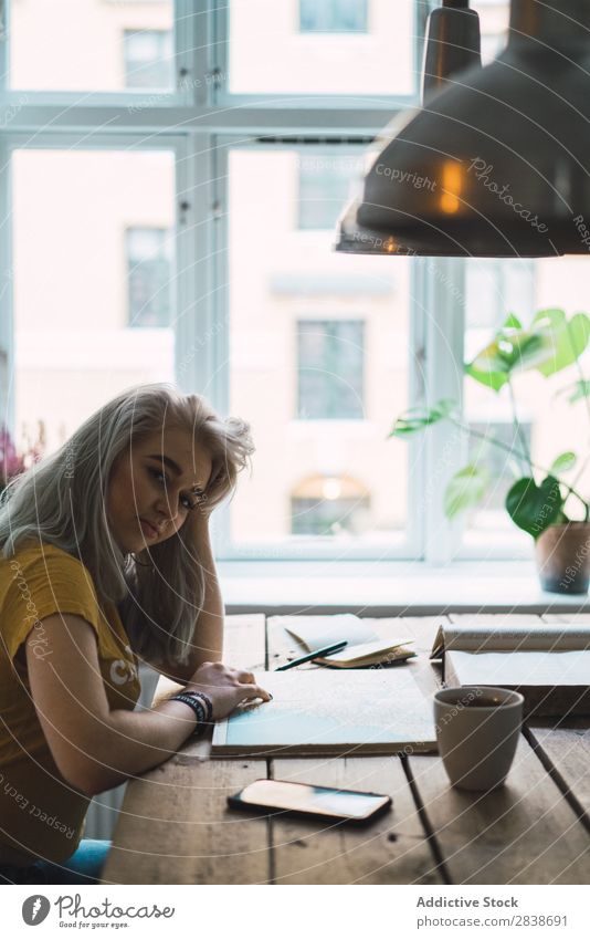 Frau mit Buch bei Tisch hübsch heimwärts Jugendliche blond besinnlich Denken sitzen Landkarte Wege & Pfade schön Lifestyle Beautyfotografie attraktiv Porträt