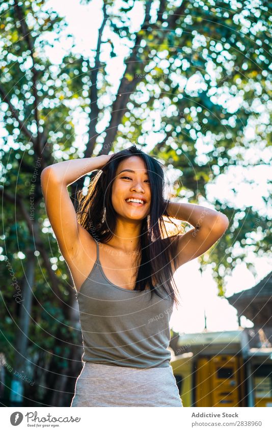 Fröhliche asiatische Frau mit brünetten Haaren hübsch Jugendliche heiter Lächeln Glück Haltehaar Freude Park Stadt schön Porträt attraktiv Beautyfotografie