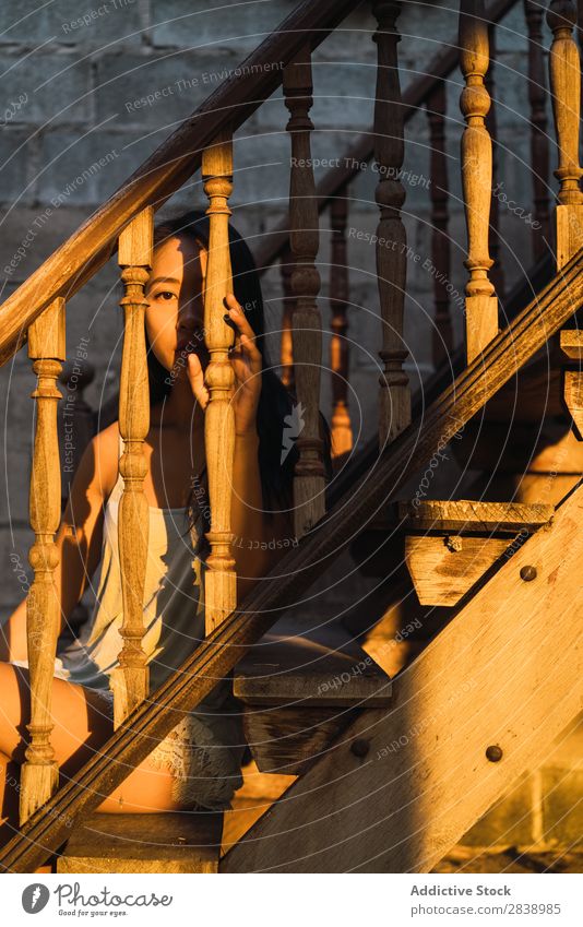 Nachdenkliche Frau auf Holztreppe hübsch asiatisch Jugendliche Geländer Freitreppe Abend Sonnenuntergang sitzen Fürsorge besinnlich schön Porträt attraktiv