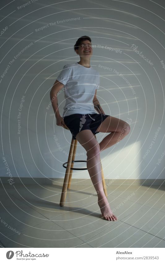 Junge Frau sitzt auf einem Hocker Stil schön Leben Wohnung Jugendliche Beine 18-30 Jahre Erwachsene T-Shirt Shorts Barfuß brünett kurzhaarig Lichtstreifen