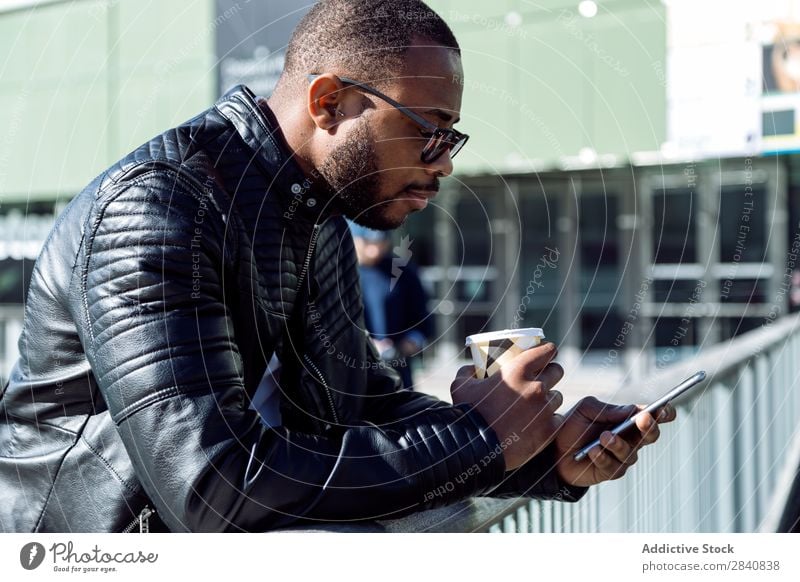 Seitenansicht eines jungen Mannes, der mit Kaffee und Telefon in der Nähe eines Metallzauns steht. männlich gelungen stylisch Selbstvertrauen Geschäftsmann
