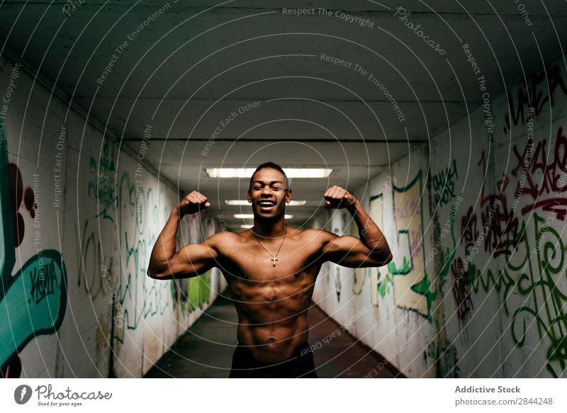 Fröhlicher Sportler, der unter Tage posiert. Mann schäbig sportlich Muskulatur zeigen ohne Hemd Afrikanisch Graffiti U-Bahn gutaussehend Torso Model Körper