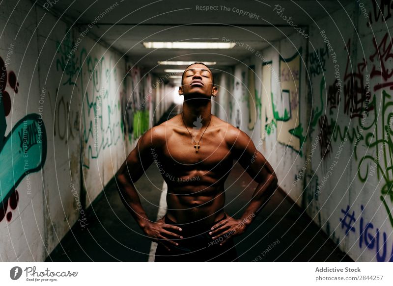 Fröhlicher Sportler, der unter Tage posiert. Mann schäbig sportlich Muskulatur zeigen ohne Hemd Afrikanisch Graffiti U-Bahn gutaussehend Torso Model Körper