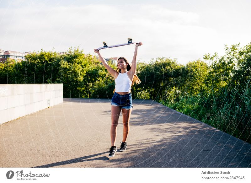 Glückliches Mädchen hält Schlittschuh über dem Kopf. Frau Skateboard heiter Freiheit Jugendliche Park ländlich Schickimicki über Kopf Skateboarding Natur