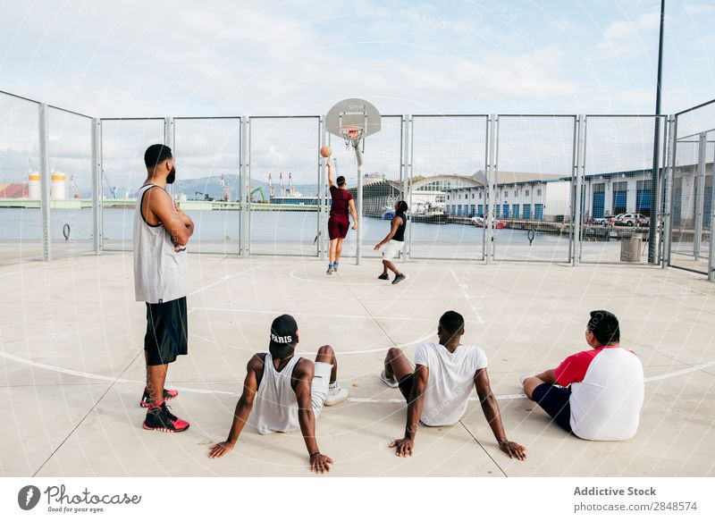 Männer, die anderen beim Basketballspielen zusehen. Mann Straßenball Spielen Sportpark beobachten sportlich Erholung Fitness Freizeit & Hobby Stadt springen