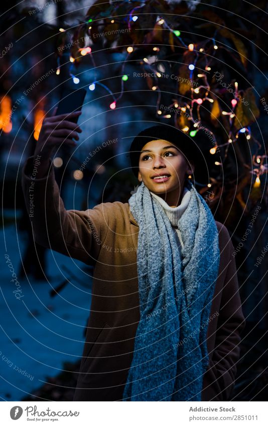 Frau, die Selfie in der Nähe eines Baumes mit Lichtern nimmt. schön Jugendliche Porträt Mensch PDA lässig Mobile Lächeln hübsch Freizeit & Hobby Handy