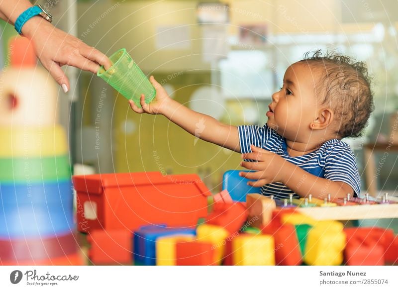 Frohes Baby, das Wasser trinkt und spielt. Spielen Kinderbetreuung Kindergarten Schule Spielzeug Kleinkind Mädchen klein Blöcke Glück Fürsorge Etage niedlich