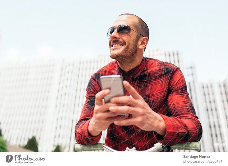 Junger Mann benutzt sein Handy auf der Straße. Mobile Porträt Glück Fahrrad Fixie Lächeln Telefon Schickimicki Lifestyle stehen benutzend Großstadt Solarzelle
