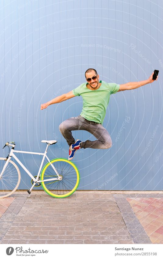 Outdoor-Porträt des schönen Springens. Mann springen Freude Lächeln Fahrrad Fixie Telefon Schickimicki Lifestyle stehen Fahrradfahren Großstadt Stadt Mensch