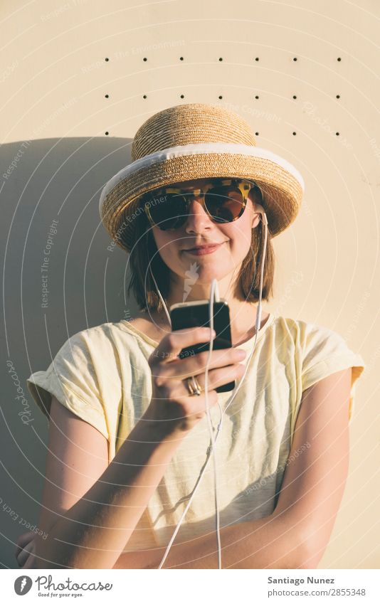 Schöne junge Hipsterin kaukasische Frau mit Smartphone und Kopfhörern, SMS und Musik hören. schön lässig Kaukasier Solarzelle Handy Chatten Mädchen Glück Hut