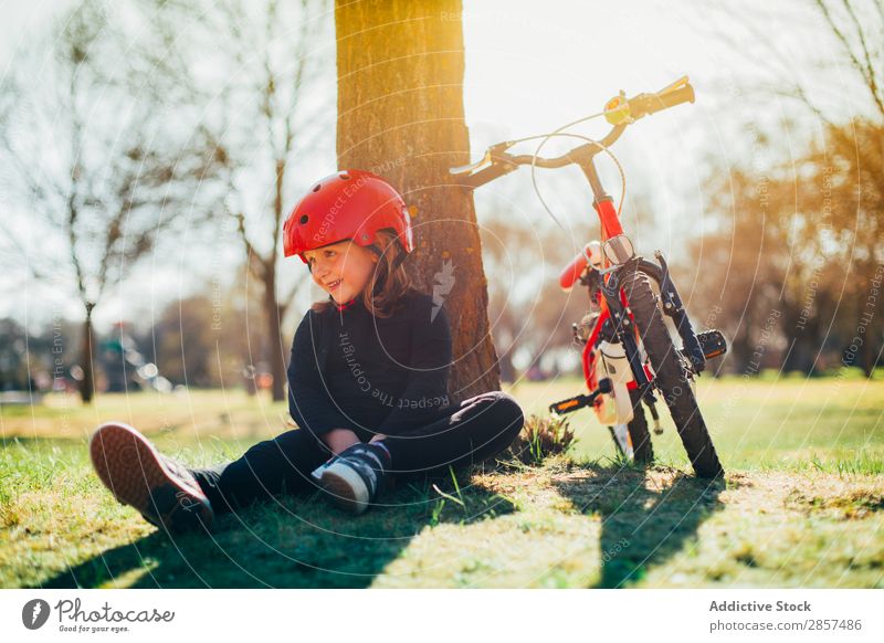 Mädchen ruht sich nach dem Radfahren aus. Fahrrad Kaukasier Kind Landschaft niedlich Freude Glück Helm Lifestyle Außenaufnahme Park Reiten Sport Sonnenuntergang