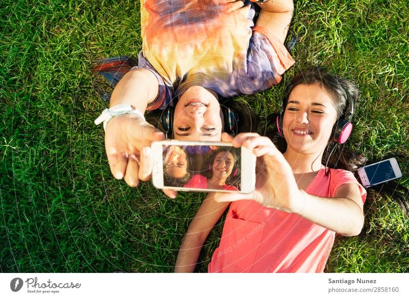 Zwei Teenager-Mädchen nehmen Selfie In Park mit. Amerikaner attraktiv schön Halterung Kaukasier Solarzelle Handy Frau Freundschaft Freude Gras Glück Kopfhörer