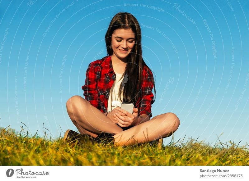 Fröhliches Teenager-Mädchen mit Handy im Park Amerikaner attraktiv schön Halterung Kaukasier Solarzelle Kommunikation Frau Freundschaft Freude Gras Glück