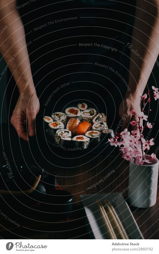 Mann mit Sushi an der Tafel serviert asiatisch Avocado Essstäbchen Speise Fisch Blume Lebensmittel Ingwer Hand Halt Japaner maki Nigiri nori roh Reis Lachs