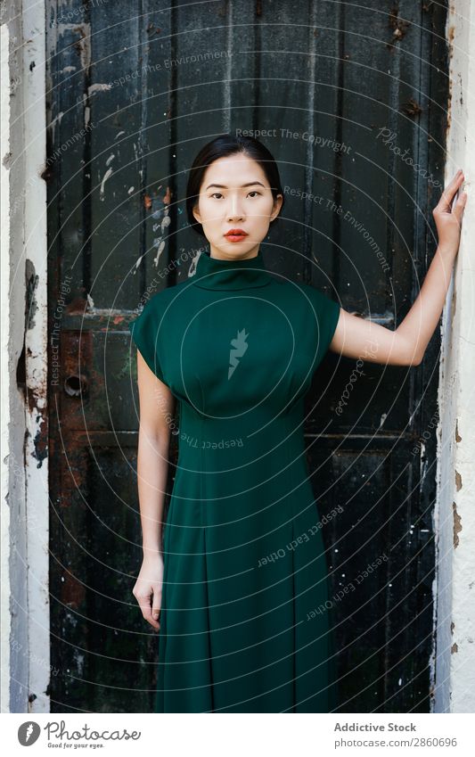 Asiatin, die sich an die Wand lehnt. Frau Jugendliche attraktiv Kleid grün asiatisch Japaner anlehnen Blick in die Kamera versteckend schön Beautyfotografie