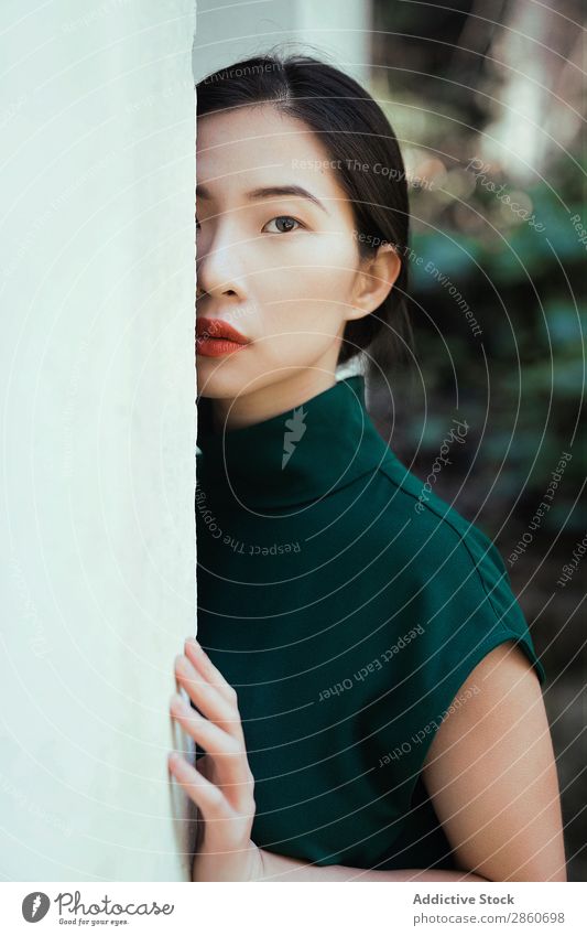 Asiatin, die sich an die Wand lehnt. Frau Jugendliche attraktiv Kleid grün asiatisch Japaner anlehnen Blick in die Kamera versteckend schön Beautyfotografie