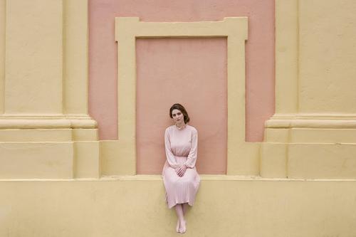 Frau in rosa Kleid, die an der Wand posiert. hübsch Jugendliche altehrwürdig Körperhaltung sitzen schön attraktiv Mensch Beautyfotografie Erwachsene Stil